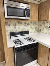 Kitchen with stainless steel microwave, range with gas stovetop, wood finish cabinets, light countertops, and wallpapered walls