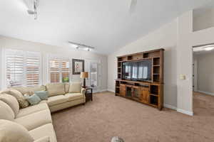 Living room with rail lighting, light colored carpet, vaulted ceiling, and a ceiling fan