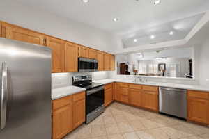 Kitchen with stainless steel appliances, vaulted ceiling, wood finish cabinetry, light tile patterned floors, and track lighting