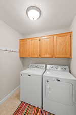 Laundry area featuring cabinet space, washer and dryer, light tile patterned floors, and a textured ceiling