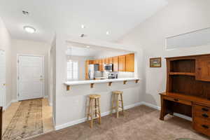 Kitchen with a kitchen bar, light countertops, a peninsula, lofted ceiling, and stainless steel appliances