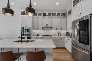 Kitchen with stainless steel appliances, glass insert cabinets, light wood finished floors, light stone countertops, and a breakfast bar