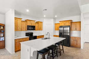 Kitchen with black appliances, a kitchen bar, a kitchen island with sink, decorative backsplash, and light stone counters