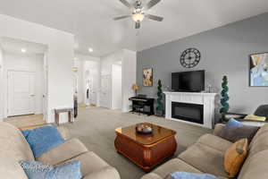 Living room featuring a ceiling fan, light colored carpet, and a glass covered fireplace