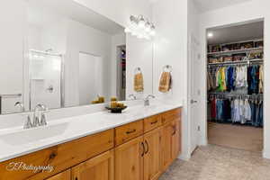 Full bathroom featuring a walk in closet, double vanity, and a shower stall