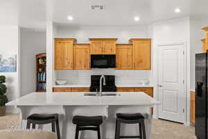 Kitchen featuring a kitchen bar, black appliances, a kitchen island with sink, light stone counters, and backsplash