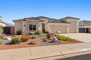 View of front of property featuring a garage, stucco siding, concrete driveway, a tiled roof, and stone siding