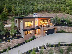 Contemporary home featuring concrete driveway, a view of trees, an attached garage, and a standing seam roof