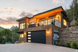 Contemporary house with concrete driveway, an attached garage, stone siding, and a balcony