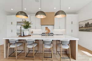 Two tone kitchen with light wood finished floors, a spacious island, stainless steel built in fridge, a kitchen bar, and two tone color scheme