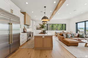 Kitchen featuring high quality appliances, beam ceiling, a kitchen island, open floor plan, and light wood finished floors