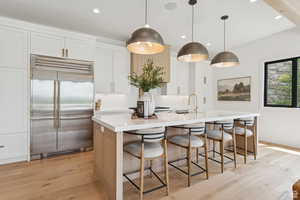 Kitchen with stainless steel built in refrigerator, light wood-style flooring, a large island with sink, pendant lighting, and a kitchen breakfast bar