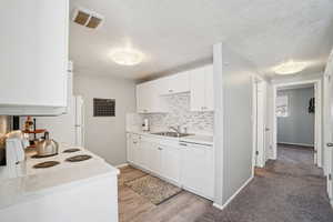 Kitchen with white cabinets, light countertops, white appliances, decorative backsplash, and a textured ceiling