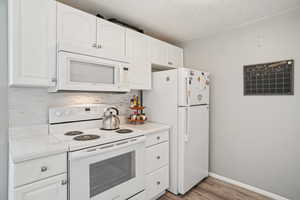 Kitchen featuring white appliances, light countertops, white cabinetry, light wood-style floors, and decorative backsplash