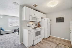 Kitchen with white appliances, light countertops, white cabinetry, decorative backsplash, and light wood-type flooring