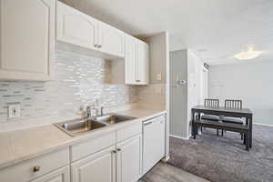 Kitchen featuring light countertops, white cabinetry, white dishwasher, a textured ceiling, and decorative backsplash