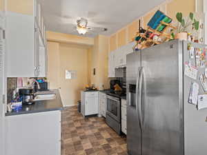 Kitchen featuring stainless steel appliances, white cabinetry, dark countertops, ceiling fan in East unit