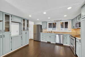 Kitchen featuring stainless steel appliances, glass fronted cabinets, light countertops, dark wood finished floors, and a textured ceiling
