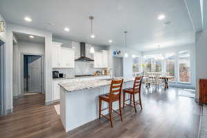 Kitchen with light stone counters, white cabinets, dark wood-style floors, a center island with sink, and a kitchen breakfast bar