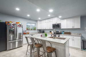 Kitchen with light stone countertops, stainless steel appliances, white cabinets, a breakfast bar area, and a center island with sink