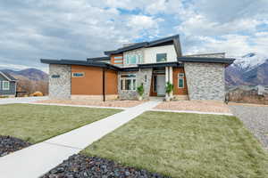 Contemporary home with a mountain view, stone siding, and a front lawn