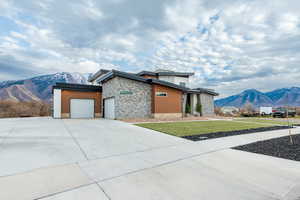 Modern home featuring a mountain view, stone siding, a garage, a front yard, and driveway