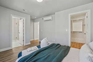 Bedroom with a spacious closet, light wood finished floors, ensuite bath, and a textured ceiling