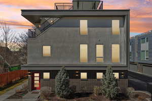Back of property at dusk featuring brick siding, a balcony, and stucco siding