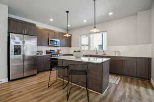 Kitchen featuring dark wood finish cabinets, a kitchen breakfast bar, a kitchen island, stainless steel appliances, and hanging light fixtures
