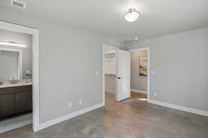 Unfurnished bedroom with finished concrete floors, ensuite bathroom, and a spacious closet