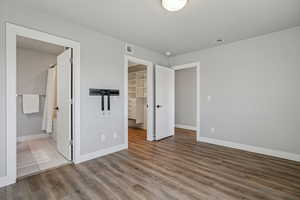 Unfurnished bedroom with a walk in closet, wood finished floors, and ensuite bathroom