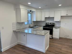 Kitchen with backsplash, electric stove, light stone countertops, white cabinetry, and a peninsula