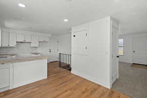 Kitchen featuring white cabinetry, light wood-type flooring, decorative backsplash, and light stone countertops
