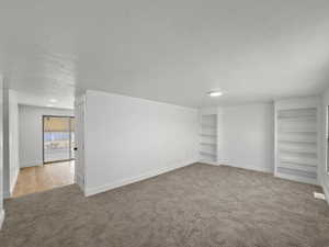 Below grade area featuring a textured ceiling, built in features, and light carpet