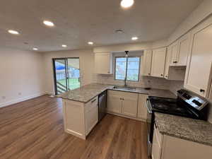 Kitchen with stainless steel appliances, light stone counters, dark wood-type flooring, white cabinets, and backsplash