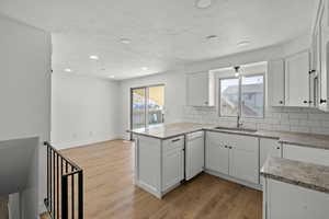 Kitchen featuring white cabinetry, light stone counters, light wood-style flooring, a peninsula, and recessed lighting