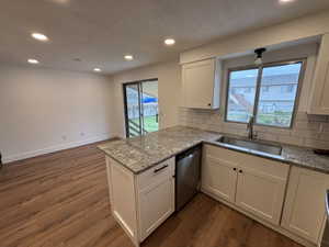 Kitchen featuring tasteful backsplash, light stone countertops, dark wood-style flooring, dishwasher, and white cabinets