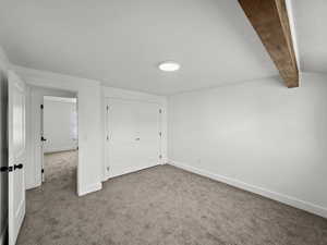 Unfurnished bedroom featuring dark carpet, beam ceiling, and a closet