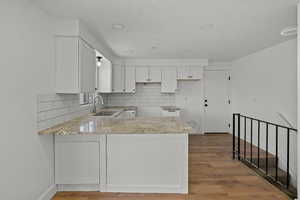 Kitchen with a peninsula, white cabinetry, light wood-style floors, and backsplash
