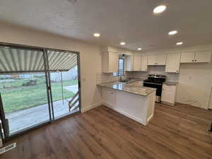 Kitchen featuring stainless steel electric range oven, white cabinetry, light stone counters, a peninsula, and dark wood-type flooring