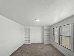 Unfurnished bedroom with dark carpet, a textured ceiling, and multiple closets