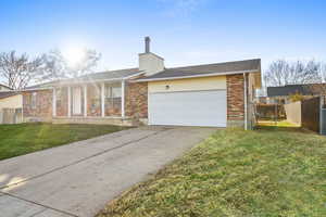 Single story home featuring concrete driveway, an attached garage, a chimney, brick siding, and a shingled roof