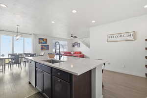 Kitchen with open floor plan, a kitchen island with sink, pendant lighting, light wood floors, and light quartz counters