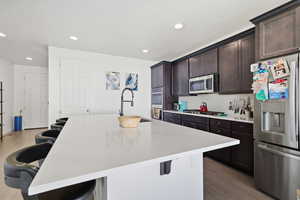 Kitchen featuring a kitchen breakfast bar, stainless steel appliances, dark wood finish cabinets, wood floors, and recessed lighting