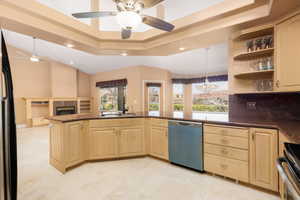 Kitchen with light wood finish cabinetry, a raised ceiling, dishwashing machine, stainless steel range, and a ceiling fan
