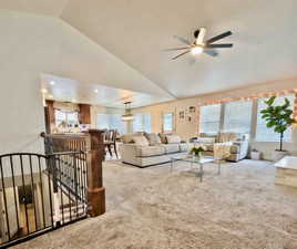 Carpeted living area with a ceiling fan, vaulted ceiling, and suspended lighting