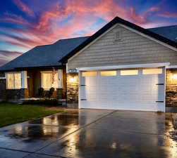View of front facade with stone siding, driveway, an attached garage, and covered porch