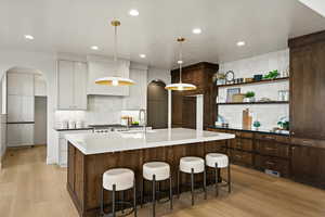Kitchen with arched walkways, two tone cabinetry, a kitchen bar, light wood-style flooring, and a spacious island