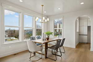 Dining space with arched walkways, light wood finished floors, and a chandelier