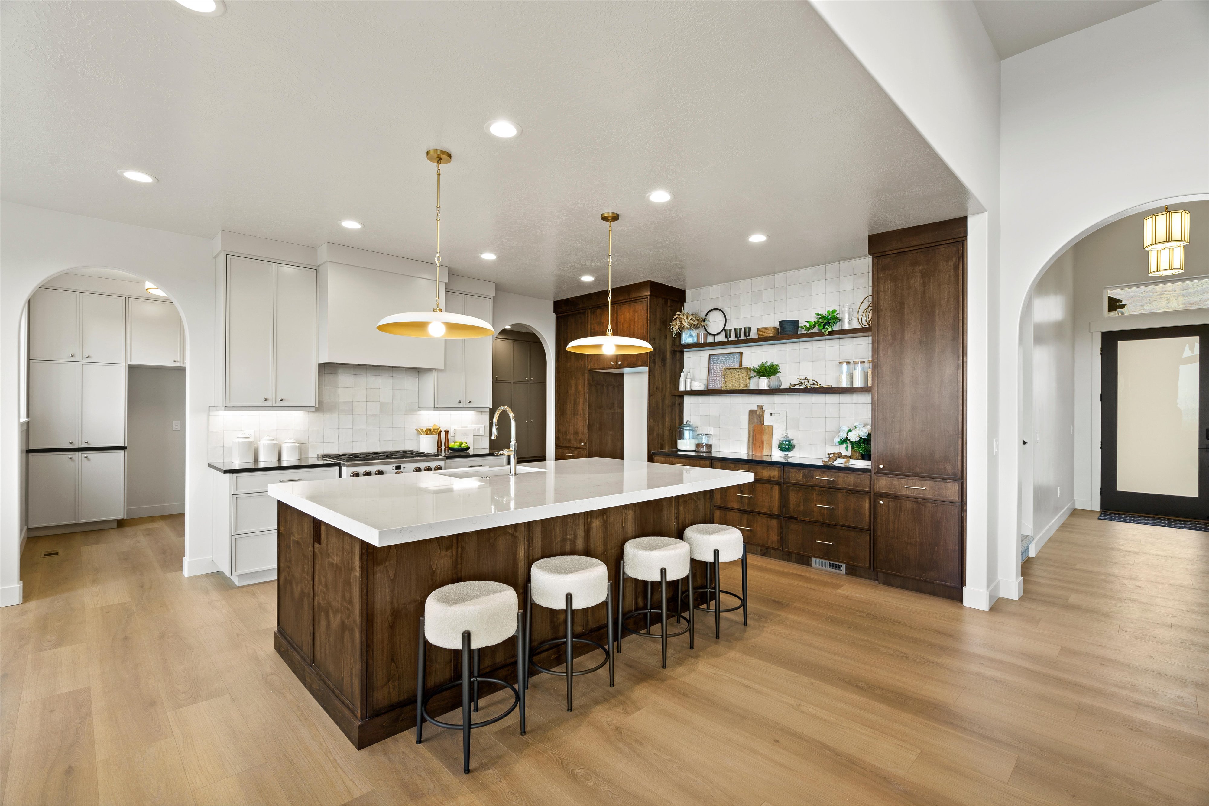 Two tone kitchen with arched walkways, two tone cabinetry, a kitchen bar, light wood-style flooring, and a large island